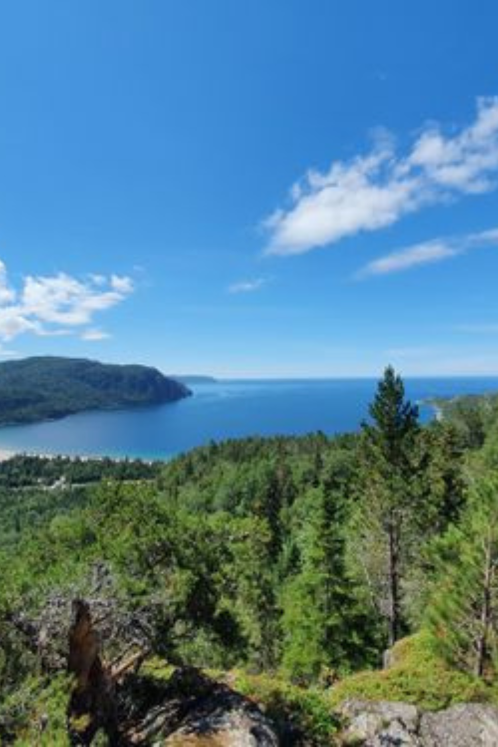 Hikers ascending a rugged trail with panoramic views of Lake Superior and surrounding verdant landscapes.